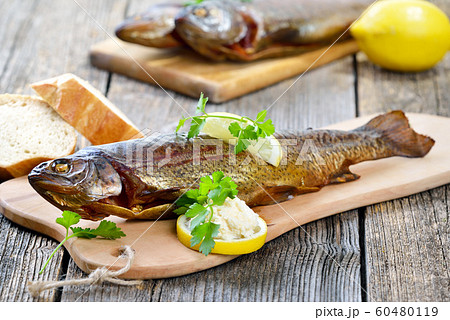 A smoked rainbow trout served on a wooden cutting board with horseradish, parsley,lemon and baguette 60480119