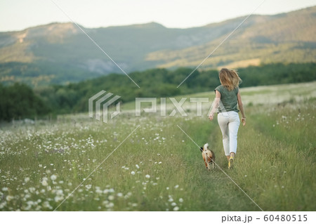 A dog and a woman running through a field of green grass A dog and a woman running through a field of green grass 60480515