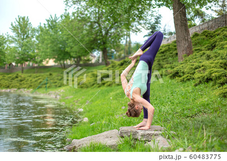A young sports girl practices yoga on a green lawn 60483775