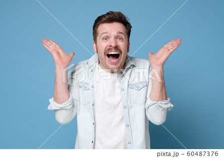 Excited casual man with mustache standing with raised hands and looking at camera being happy. 60487376