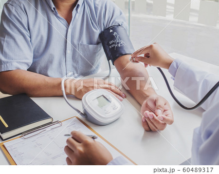 The doctor evaluates the patient with a stethoscope, blood pressure monitor and records the results 60489317