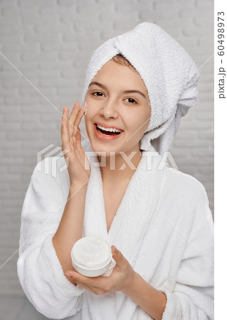 Portrait of happy female in towel applying cream face 60498973