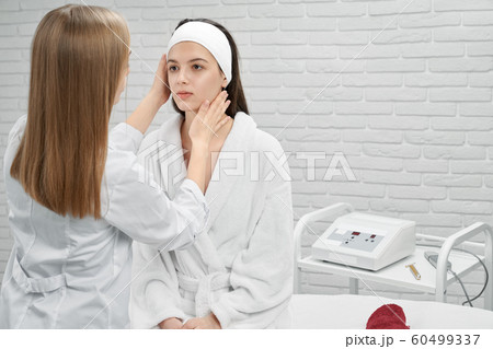 Woman sitting on coach while beautician looking at face 60499337