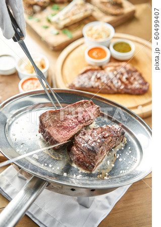 The waiter is butchering griled meat with a knife. Grilled fillet steaks with Pickled cabbage and two sauces.. Barbecue restaurant menu. 60499407