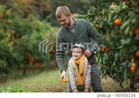 A child a boy and a man in warm sweaters smile and look at the camera on the street in a garden with trees A child a boy and a man in warm sweaters smile and look at the camera on the street in a garden with trees 60500138