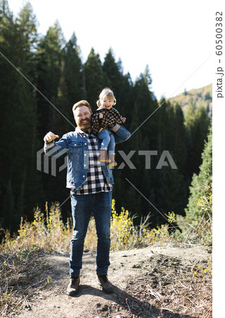 Father carrying his daughter on his shoulders by forest 60500382