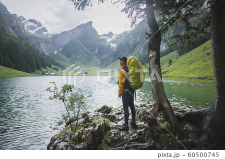 Woman wearing yellow backpack by Seealpsee lake in Appenzell Alps, Switzerland 60500745