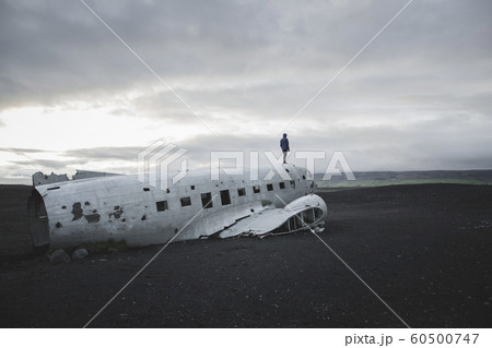 Man standing on abandoned airplane in black sand desert 60500747