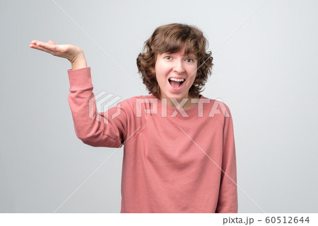 Positive curly woman showing on copyspace with happy expression on face. 60512644