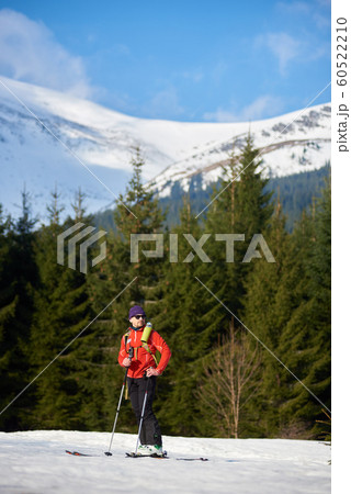 Male skier on skis on background of spruce trees and snowy mountain peak on frosty sunny winter day. Male skier on skis on background of spruce trees and snowy mountain peak on frosty sunny winter day. 60522210