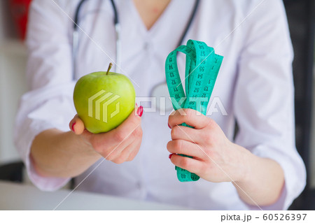 Diet. Fitness and healthy food diet concept. Balanced diet with vegetables. Portrait of cheerful doctor nutritionist measuring green apple in her office. Concept of natural food and healthy lifestyle Diet. Fitness and healthy food diet concept. Balanced diet with vegetables. Portrait of cheerful doctor nutritionist measuring green apple in her office. Concept of natural food and healthy lifestyle 60526397