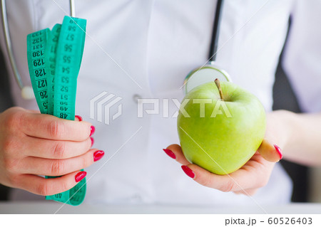 Diet. Fitness and healthy food diet concept. Balanced diet with vegetables. Portrait of cheerful doctor nutritionist measuring green apple in her office. Concept of natural food and healthy lifestyle Diet. Fitness and healthy food diet concept. Balanced diet with vegetables. Portrait of cheerful doctor nutritionist measuring green apple in her office. Concept of natural food and healthy lifestyle 60526403