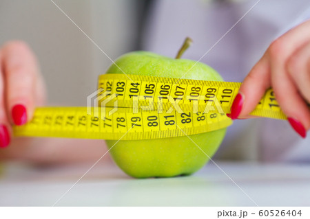 Diet. Fitness and healthy food diet concept. Balanced diet with vegetables. Portrait of cheerful doctor nutritionist measuring green apple in her office. Concept of natural food and healthy lifestyle Diet. Fitness and healthy food diet concept. Balanced diet with vegetables. Portrait of cheerful doctor nutritionist measuring green apple in her office. Concept of natural food and healthy lifestyle 60526404