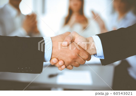 Business people shaking hands at meeting while theirs colleagues clapping and applauding. Group of unknown businessmen and women in modern white office. Success teamwork, partnership and handshake Business people shaking hands at meeting while theirs colleagues clapping and applauding. Group of unknown businessmen and women in modern white office. Success teamwork, partnership and handshake 60543021
