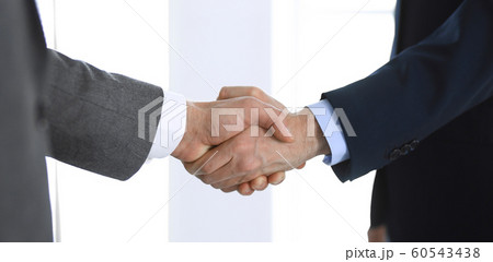 Business people shaking hands while standing with colleagues after meeting or negotiation, close-up. Group of unknown businessmen and women in modern office. Teamwork, partnership and handshake Business people shaking hands while standing with colleagues after meeting or negotiation, close-up. Group of unknown businessmen and women in modern office. Teamwork, partnership and handshake 60543438