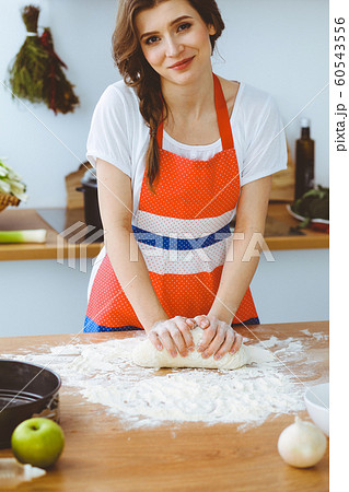 Young brunette woman cooking pizza or handmade pasta in the kitchen. Housewife preparing dough on wooden table. Dieting, food and health concept 60543556