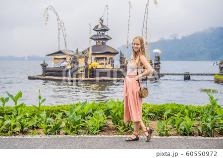 Young woman traveler in the background of Pura Ulun Danu Bratan, Bali. Hindu temple surrounded by flowers on Bratan lake, Bali. Major Shivaite water temple in Bali, Indonesia. Hindu temple Young woman traveler in the background of Pura Ulun Danu Bratan, Bali. Hindu temple surrounded by flowers on Bratan lake, Bali. Major Shivaite water temple in Bali, Indonesia. Hindu temple 60550972
