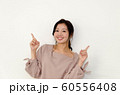 白い壁の前で両手の指で上を指し示しながら微笑む女性 60556408