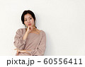 白い壁の前で顎に手を当てて考えている女性 60556411