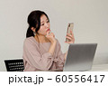 パソコンの前でスマートフォンを持ちながら不機嫌な表情をする女性 60556417