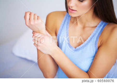 Pain hand. Sad woman with pain in hand at home 60560076