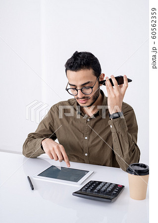 Busy young male accountant with smartphone by ear pointing at touchpad display Busy young male accountant with smartphone by ear pointing at touchpad display 60562359