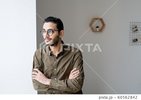 Young cross-armed businessman in eyeglasses and shirt looking through window 60562842