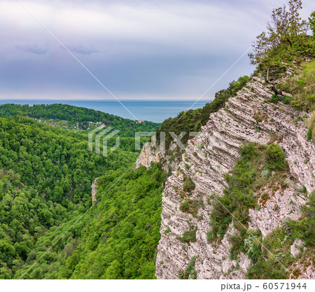 Mountain with a steep rocky slope and valley with thick green forest and the sea below Mountain with a steep rocky slope and valley with thick green forest and the sea below 60571944