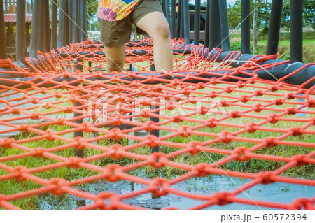 Young woman tried to walk on the bridge floor tied with a red rope to cross the swamp in the fields. Selective focus on her leg. 60572394