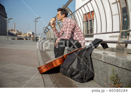 Young guy sitting outdoors with his instrument 60580284