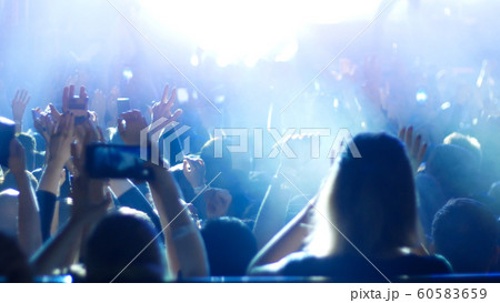 Energetic people dancing with their hands up at the rock concert and recording on the phone - blue lighting 60583659