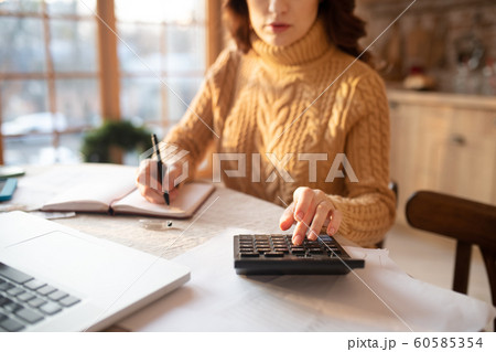 Dark-haired young woman in sweater making calculations 60585354