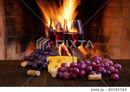 Two glasses of red wine with cheese and grapes near the fireplace. 60585584