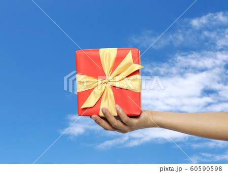 Women's hand holding a red gift box on Blue sky background. 60590598