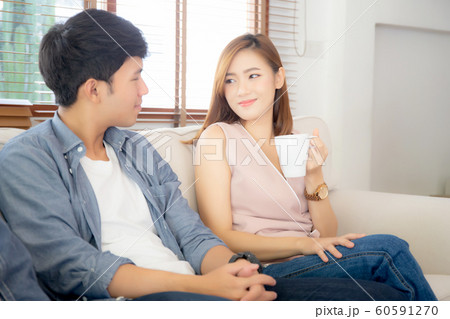 Beautiful young asian couple smiling and talking story married sitting on sofa at home together Beautiful young asian couple smiling and talking story married sitting on sofa at home together 60591270