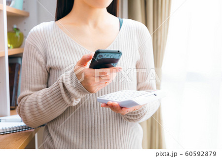 スマホを見ながら計算する女性 スマホを見ながら計算する女性 60592879