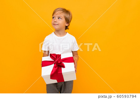 boy holds a box with a red ribbon and looks away on an orange background boy holds a box with a red ribbon and looks away on an orange background 60593794