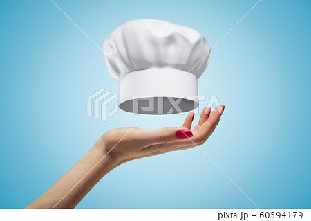 Side closeup of woman's hand facing up and levitating toque blanche on light blue gradient background. 60594179