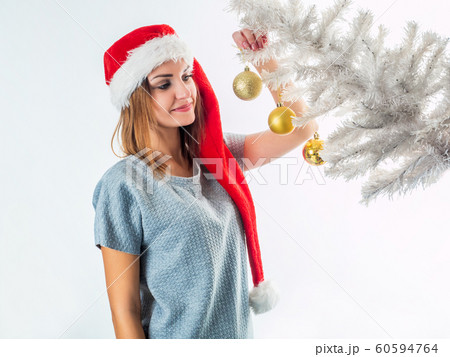 Young woman in Santa hat hanging ball on a Christmas tree 60594764