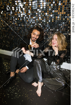 Happy young glamorous couple making selfie while sitting by glittering wall Happy young glamorous couple making selfie while sitting by glittering wall 60596242