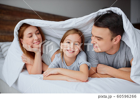 portrait of smiling parents and daughter on bed 60596266
