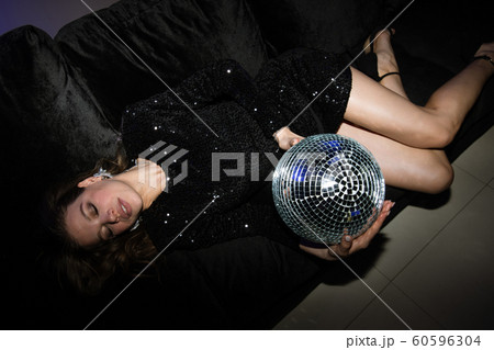 Restful young woman in black glittering dress holding disco ball 60596304