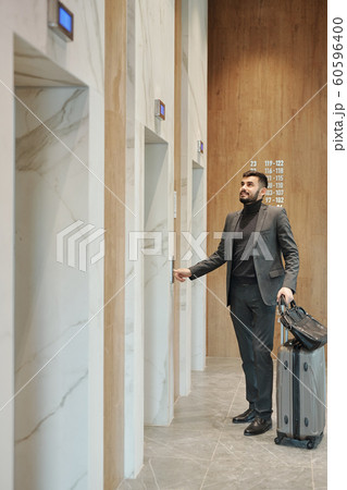 Businessman pushing button on the wall while standing by one of elevator doors Businessman pushing button on the wall while standing by one of elevator doors 60596400