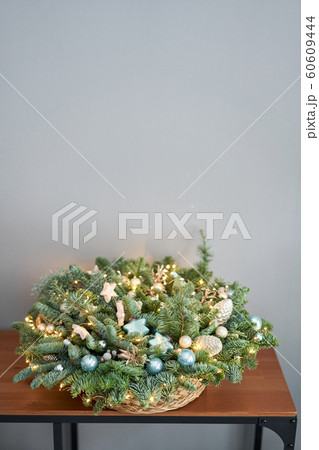 Big arrangement of fresh spruce in a wicker basket. Decorated with blue balls, cones and small stars. Christmas mood. light bulbs Garlands 60609444