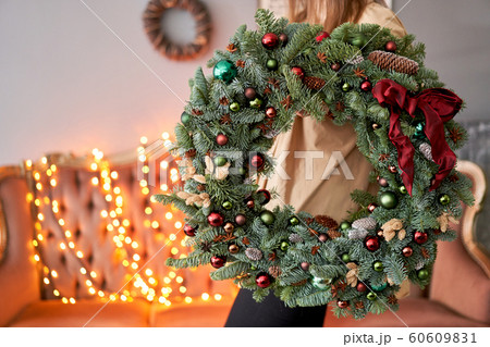 Christmas mood. Beautiful festive wreath of fresh spruce in woman hands. Xmas tree. Bokeh of Garland lights on background. 60609831