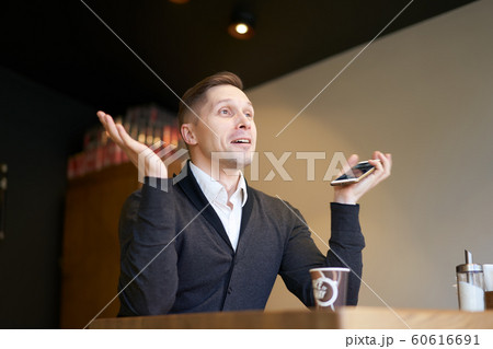 Happy businessman with phone in hands sitting at table 60616691