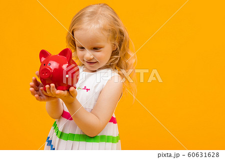 blond little girl holding with a red piggy bank on a yellow background blond little girl holding with a red piggy bank on a yellow background 60631628