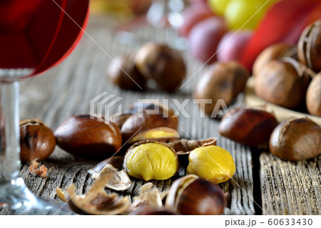 Roasted chestnuts with South Tyrolean red wine on an old wooden table, wine grapes in the background 60633430