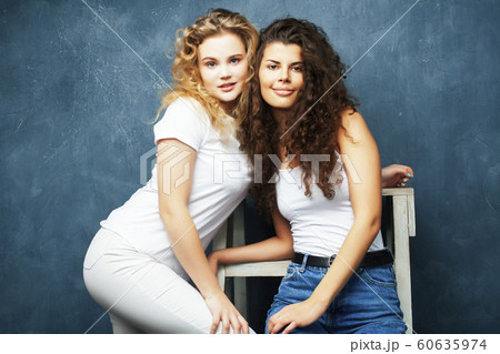 young pretty teenage girls friends with blond and brunette curly hair posing cheerful on blue background, lifestyle people concept 60635974