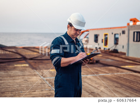 Deck Officer on deck of offshore vessel or ship , wearing PPE personal protective equipment. He fills checklist. Paperwork at sea 60637664